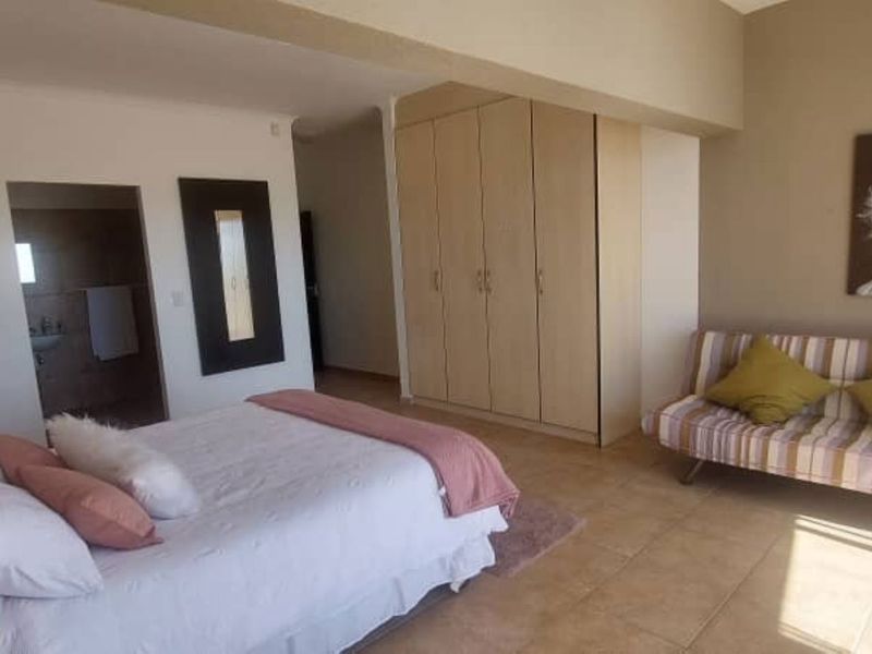 Spacious bedroom featuring built-in cupboards, tiled flooring, and direct access to an en-suite bathroom.