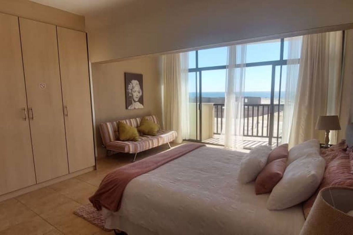 Spacious bedroom featuring built-in cupboards, tiled flooring, and large sliding glass doors that open to a balcony with ocean views.