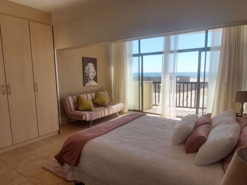 Spacious bedroom featuring built-in cupboards, tiled flooring, and large sliding glass doors that open to a balcony with ocean views.