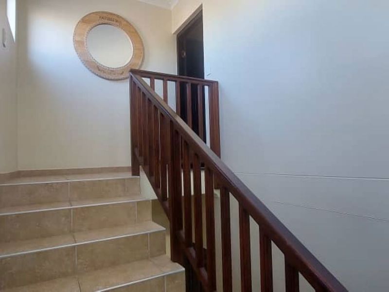A bright hallway featuring a tiled staircase with a sturdy wooden balustrade and handrail, leading to an upper level.
