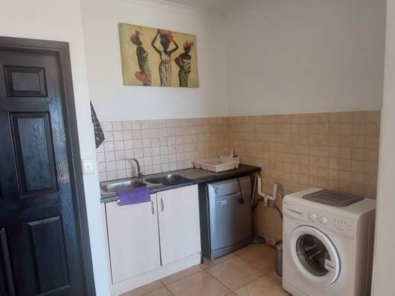 A functional laundry area featuring built-in cabinetry, a stainless steel sink, and tiled splashback, with dedicated plumbing connections for appliances.