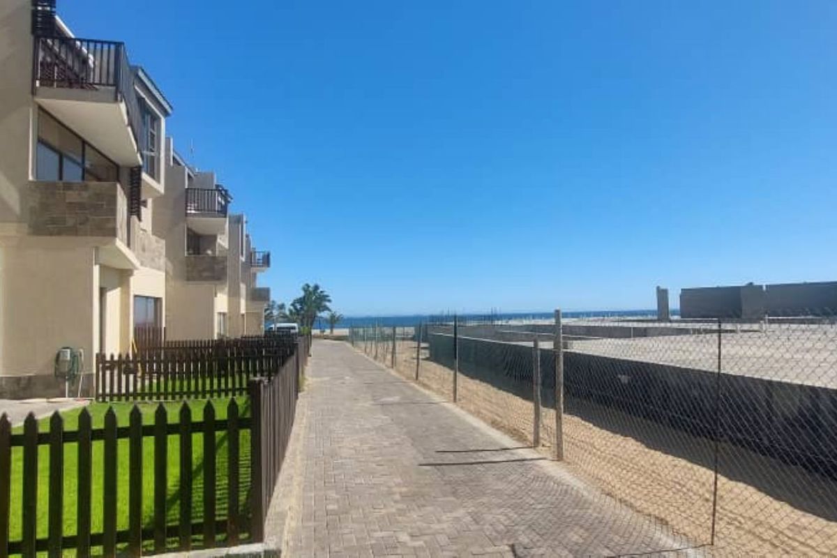 Rear view of the townhouse complex featuring private garden patches, paved walkways, and balconies overlooking the coastal area.