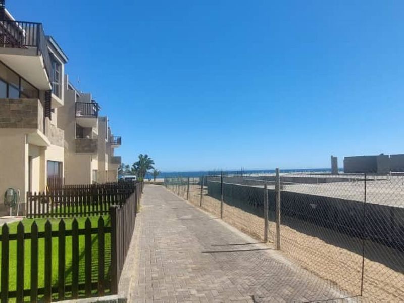 Rear view of the townhouse complex featuring private garden patches, paved walkways, and balconies overlooking the coastal area.
