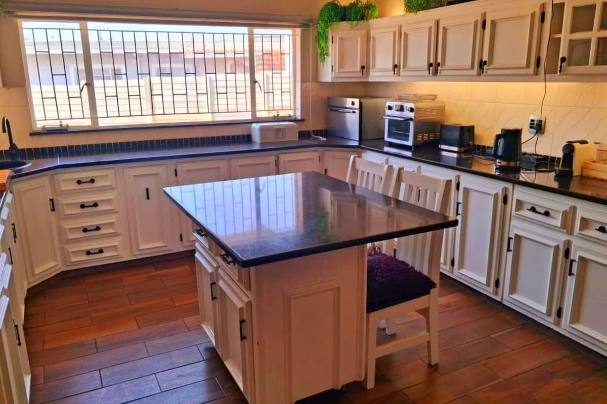 A well-maintained kitchen featuring white cabinetry, dark granite countertops, a central island, and wood-look tiled flooring with ample natural light.