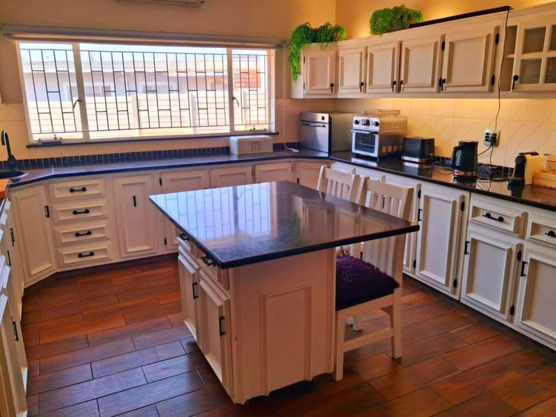 A well-maintained kitchen featuring white cabinetry, dark granite countertops, a central island, and wood-look tiled flooring with ample natural light.