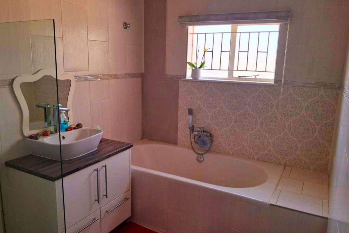 A well-maintained bathroom featuring a built-in vanity with a vessel sink, a bathtub with a handheld shower mixer, and decorative tiled wall finishes.