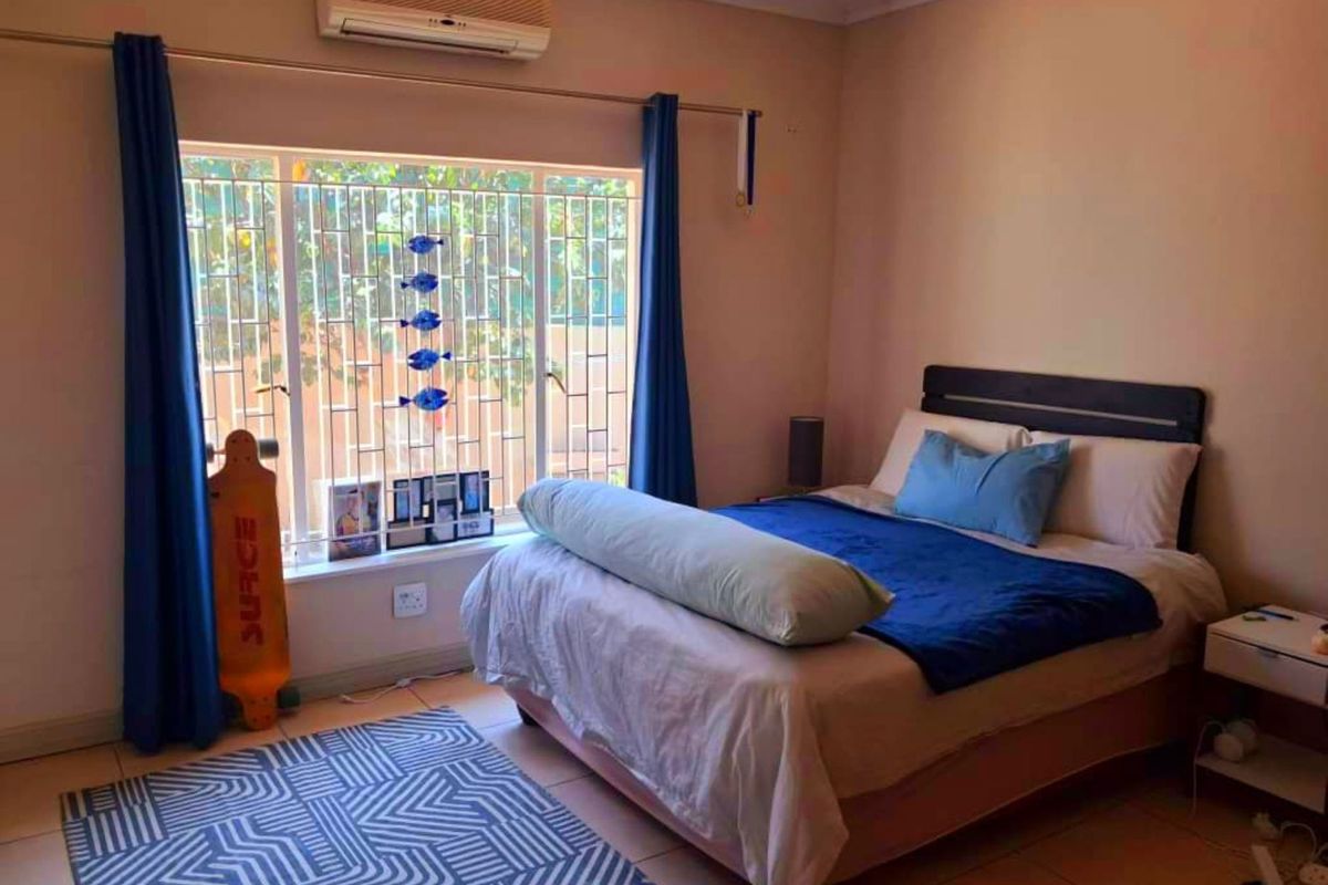 A functional bedroom featuring tiled flooring, a wall-mounted split-system air conditioner, and security bars on the window.