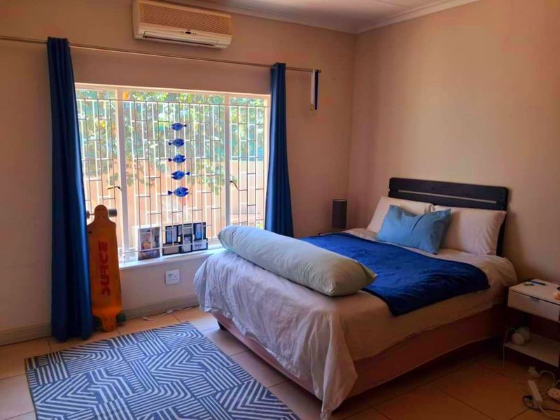 A functional bedroom featuring tiled flooring, a wall-mounted split-system air conditioner, and security bars on the window.