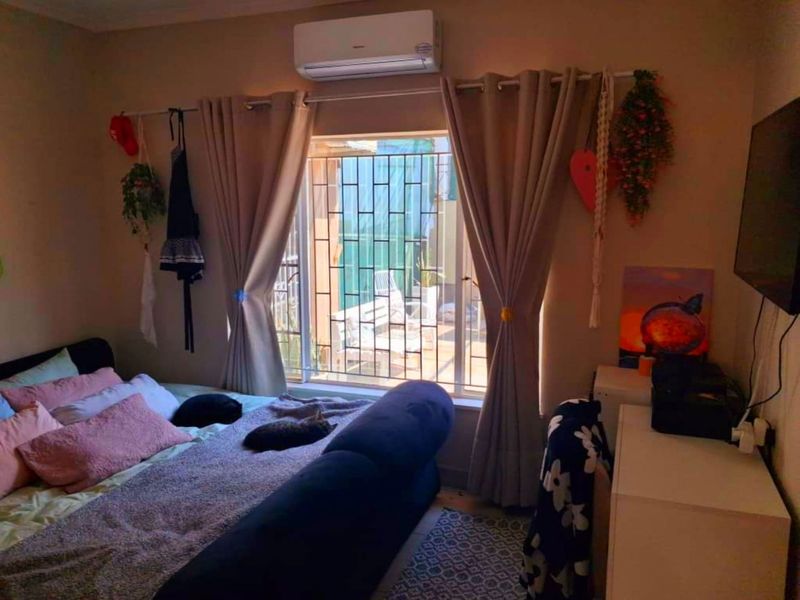 A bedroom featuring a wall-mounted split-system air conditioner and a window fitted with security bars.