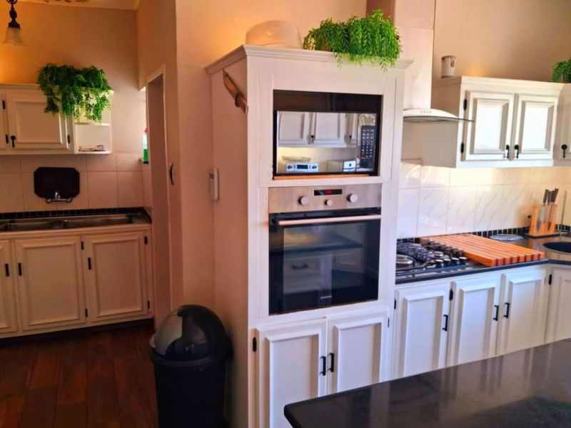 A functional kitchen featuring white shaker-style cabinetry, granite countertops, a built-in oven and microwave, and a gas hob with an extractor fan.