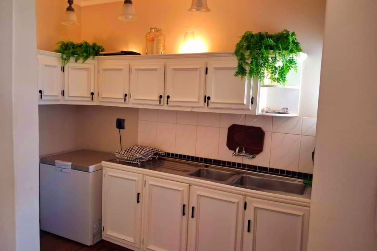 A functional scullery area featuring white built-in cabinetry, a double basin sink, and tiled backsplash, providing additional prep and wash-up space.