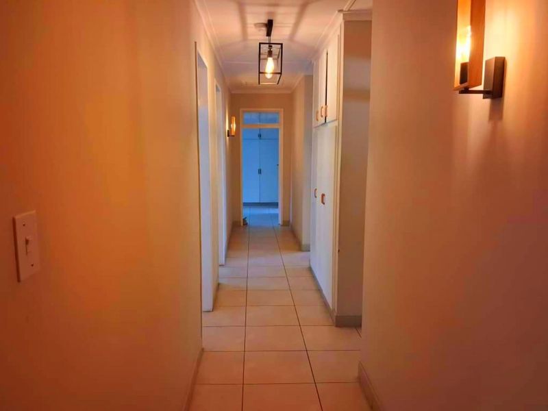 A well-lit hallway featuring tiled flooring, built-in storage cabinetry, and modern pendant and wall lighting fixtures.