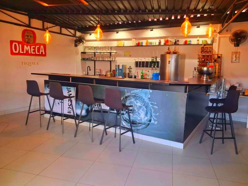 A dedicated home bar area featuring a built-in counter, sink, open shelving, and industrial-style exposed ceiling with pendant lighting.