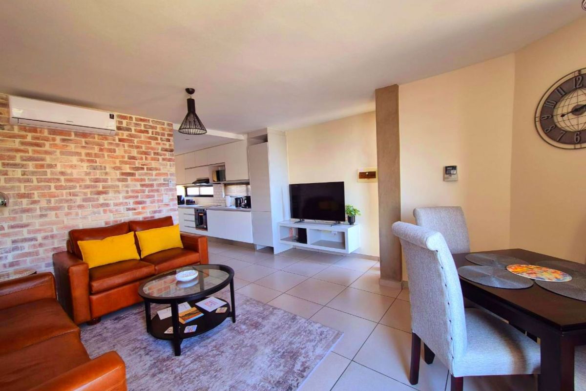 Open-plan living and dining area featuring an exposed brick wall, tiled floors, and a modern kitchen with integrated appliances.