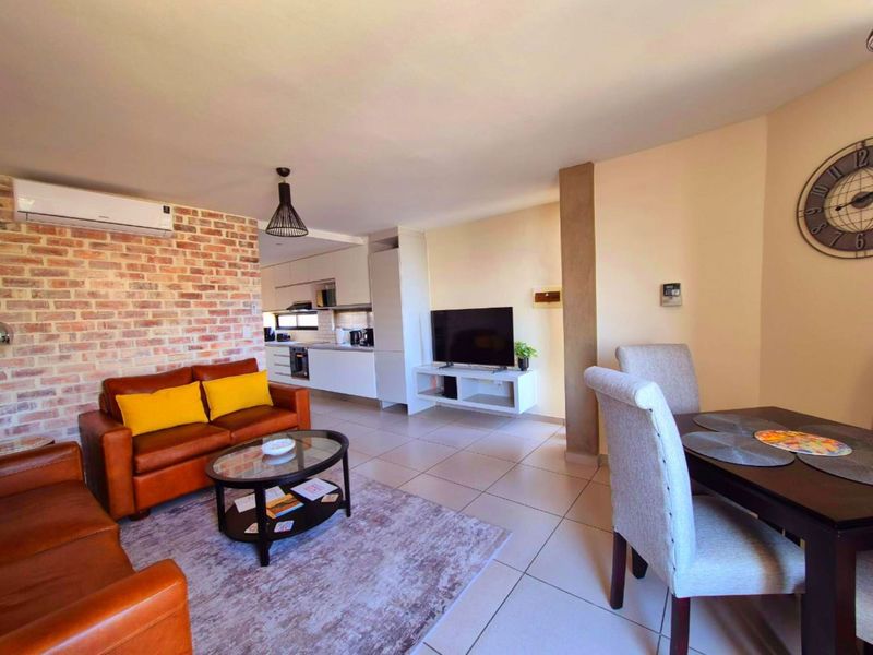 Open-plan living and dining area featuring an exposed brick wall, tiled floors, and a modern kitchen with integrated appliances.