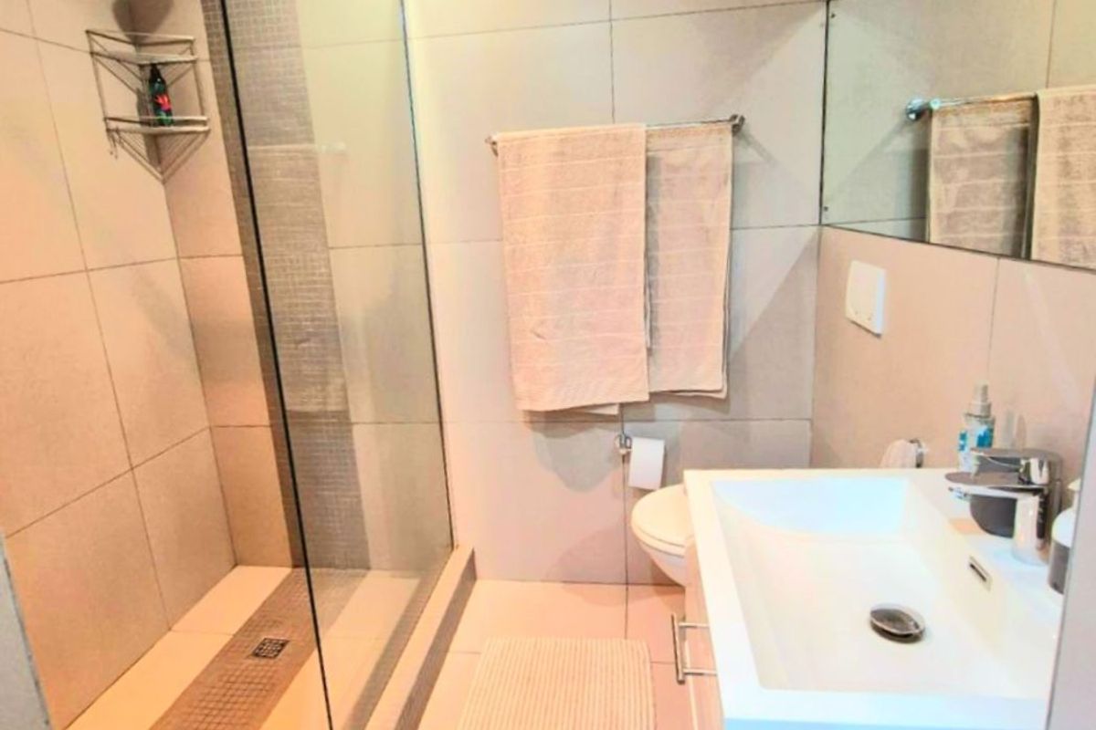 Modern bathroom featuring a glass-enclosed walk-in shower, wall-mounted vanity with basin, and large wall mirror with neutral floor-to-ceiling tiling.