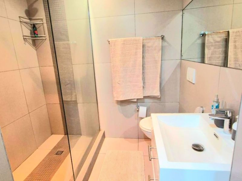 Modern bathroom featuring a glass-enclosed walk-in shower, wall-mounted vanity with basin, and large wall mirror with neutral floor-to-ceiling tiling.