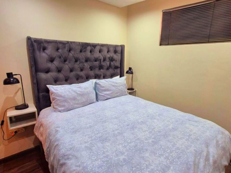 A cozy bedroom featuring dark laminate flooring, recessed ceiling lighting, and a window fitted with venetian blinds.