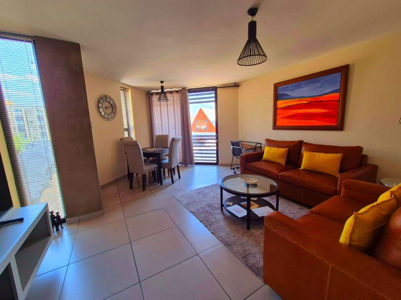 An open-plan living and dining area featuring neutral tiled flooring, modern pendant lighting, and a sliding glass door leading to an outdoor space.