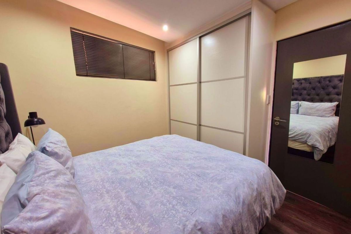 A well-maintained bedroom featuring laminate flooring, recessed lighting, and a large built-in sliding door wardrobe with a full-length mirror on the door.