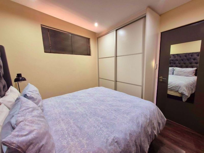 A well-maintained bedroom featuring laminate flooring, recessed lighting, and a large built-in sliding door wardrobe with a full-length mirror on the door.