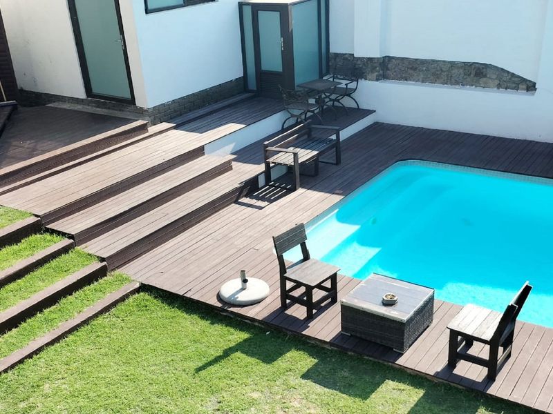 Outdoor pool area featuring extensive timber decking, a swimming pool, and stone retaining wall elements, providing a functional space for relaxation.