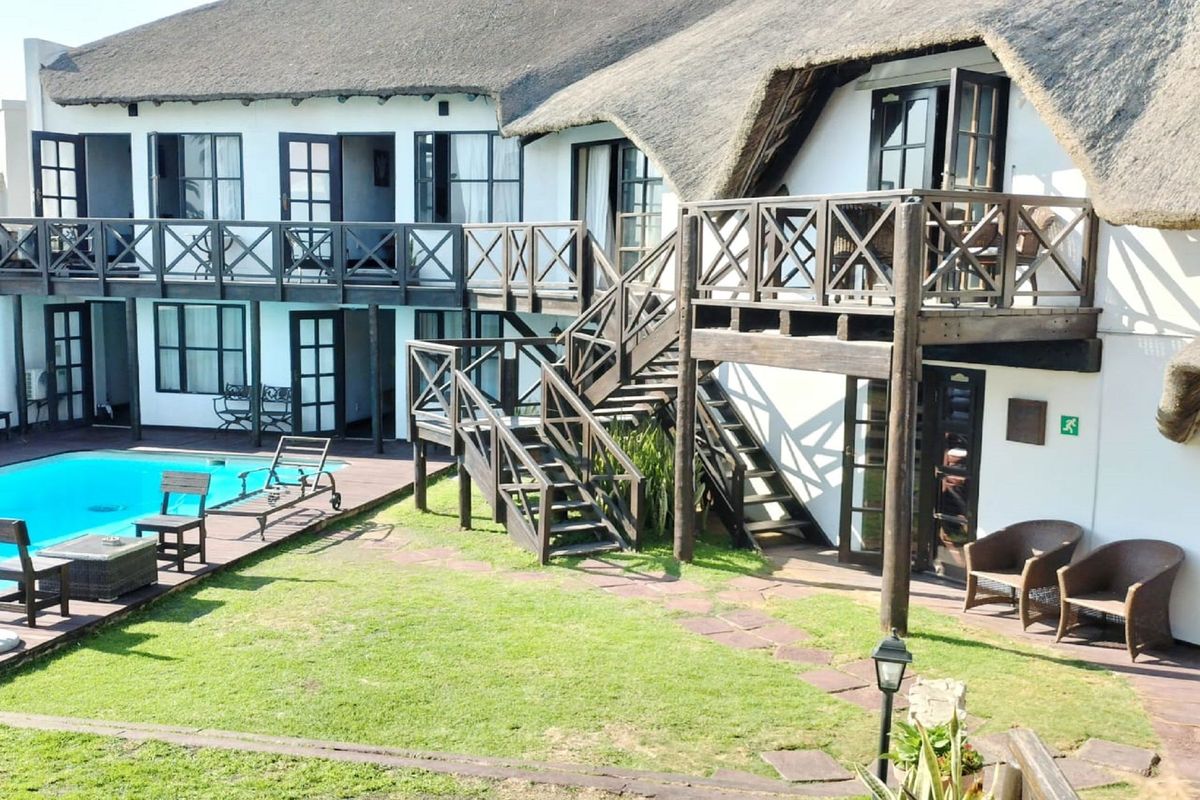 Rear view of a guest house featuring a thatched roof, swimming pool, wooden decking, and external staircases leading to upper-level balcony access.