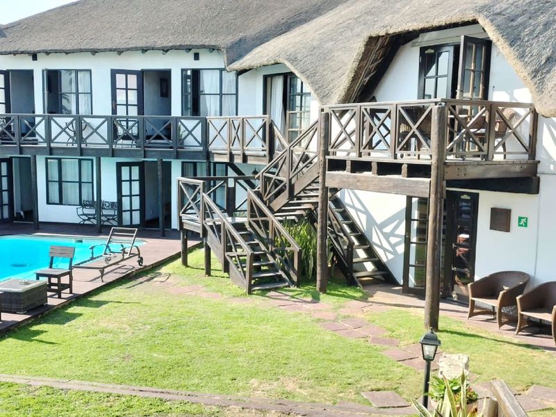 Rear view of a guest house featuring a thatched roof, swimming pool, wooden decking, and external staircases leading to upper-level balcony access.