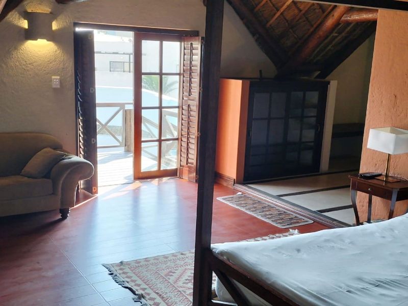 Spacious bedroom featuring a unique thatched roof with exposed timber rafters, tiled flooring, and direct access to an outdoor balcony through french doors.