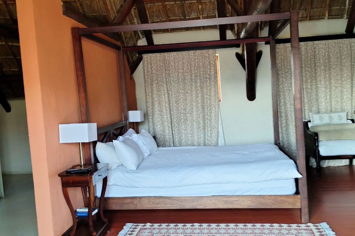 A spacious bedroom featuring a high thatched ceiling with exposed timber rafters and warm-toned walls, creating a rustic and inviting atmosphere.