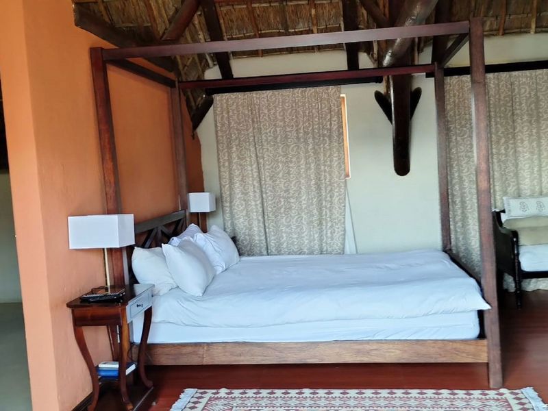 A spacious bedroom featuring a high thatched ceiling with exposed timber rafters and warm-toned walls, creating a rustic and inviting atmosphere.