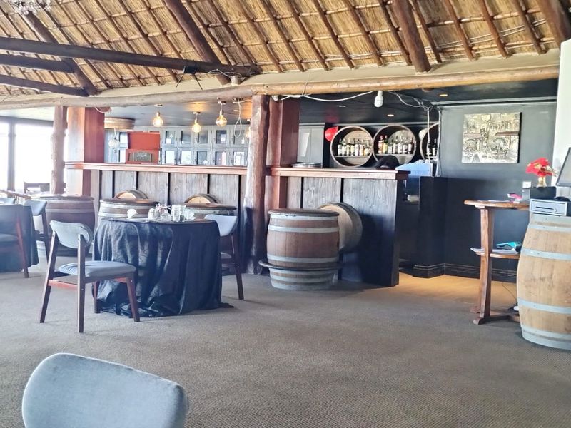 A rustic bar area featuring a traditional thatched roof, exposed timber beams, and a built-in bar counter with integrated circular shelving.