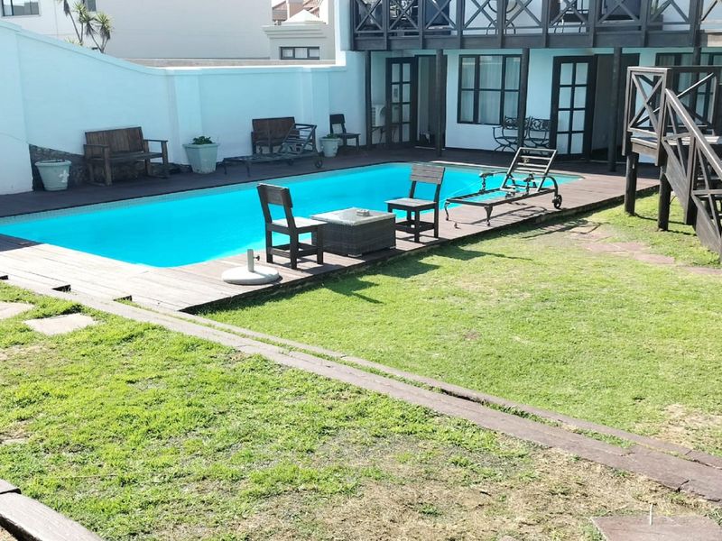 Outdoor pool area featuring a swimming pool, timber decking, and a wooden staircase leading to an upper balcony level.