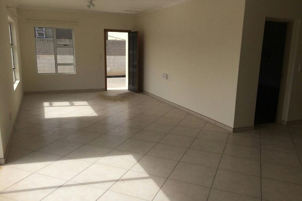A spacious, empty living area featuring neutral tiled flooring, clean walls, and natural light through aluminium-framed windows.