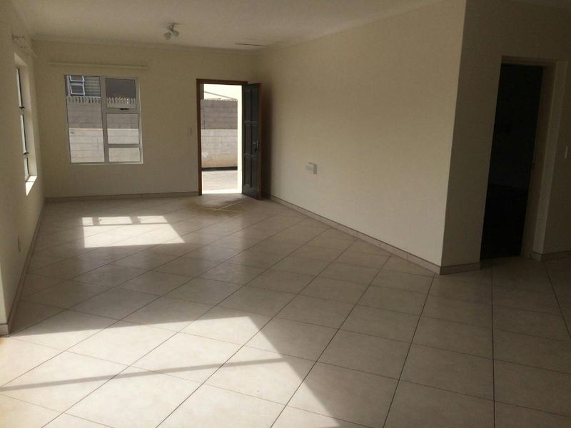 A spacious, empty living area featuring neutral tiled flooring, clean walls, and natural light through aluminium-framed windows.