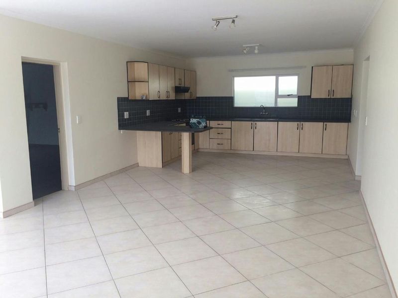 Spacious open-plan kitchen featuring light wood-finish cabinetry, dark tiled backsplash, and neutral ceramic floor tiles in a clean, vacant setting.