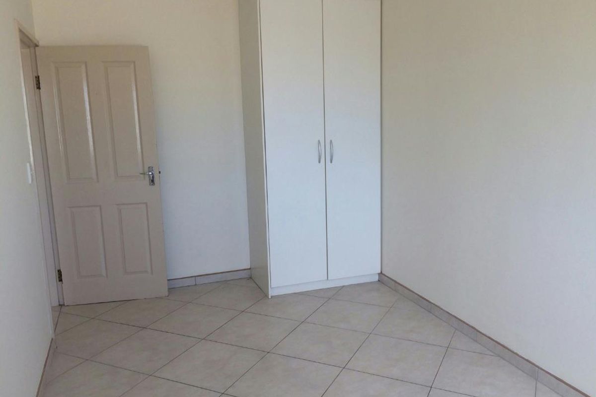 A clean, empty bedroom featuring neutral tiled flooring and a built-in white wardrobe, offering a blank canvas for personalization.