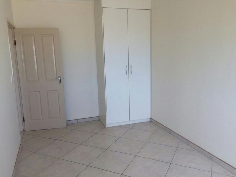 A clean, empty bedroom featuring neutral tiled flooring and a built-in white wardrobe, offering a blank canvas for personalization.