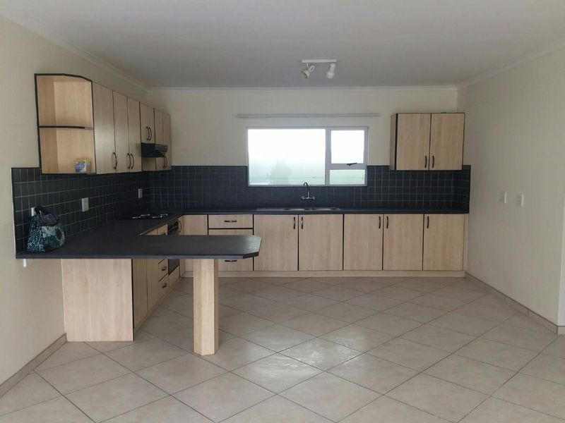 A functional kitchen featuring light wood-look cabinetry, dark tiled backsplash, built-in appliances, and tiled flooring in an open-plan layout.