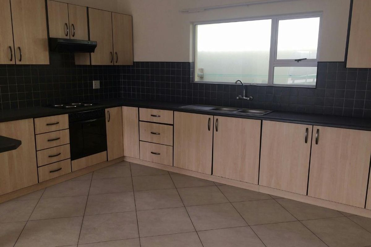 A functional kitchen featuring light wood-look cabinetry, dark tiled backsplash, built-in oven with hob, and tiled flooring in a clean, empty space.
