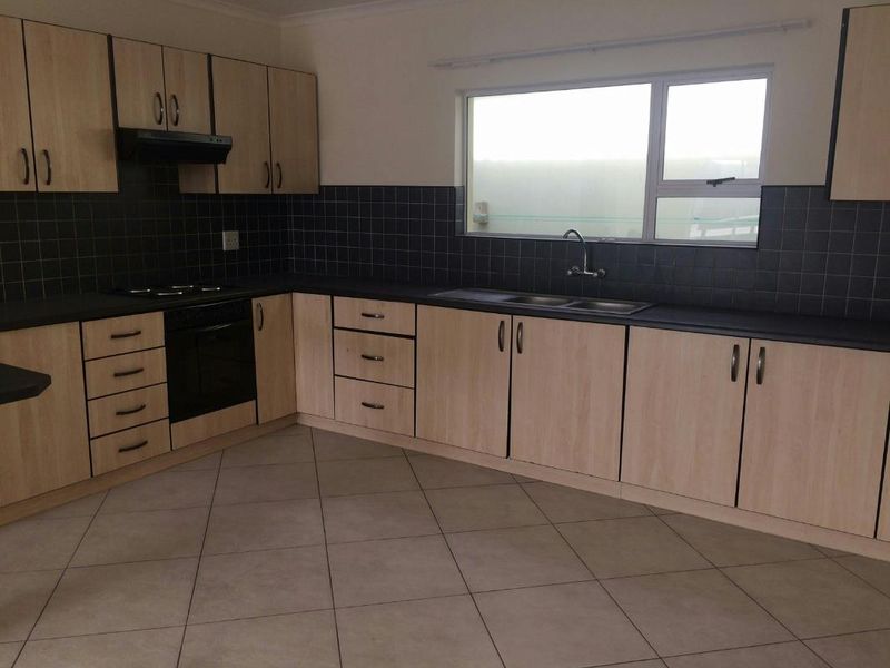 A functional kitchen featuring light wood-look cabinetry, dark tiled backsplash, built-in oven with hob, and tiled flooring in a clean, empty space.