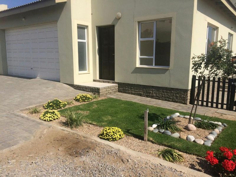 Front elevation of a townhouse featuring a paved driveway, single garage, and a well-maintained landscaped garden with stone accents.