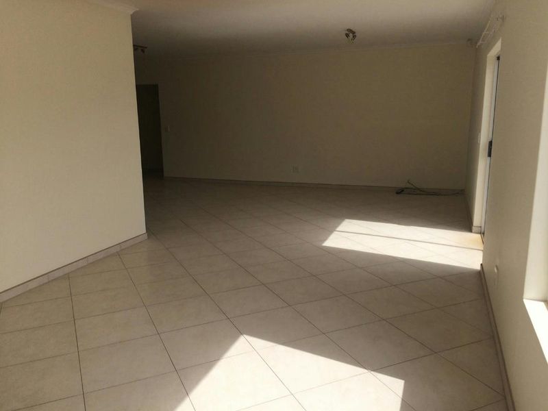 A spacious, empty open-plan living area featuring neutral tiled flooring and a sliding glass door providing natural light.