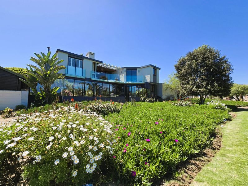 Rear view of a modern two-story residence featuring extensive glass facades, an upper-level balcony with glass balustrades, and a well-maintained landscaped garden.