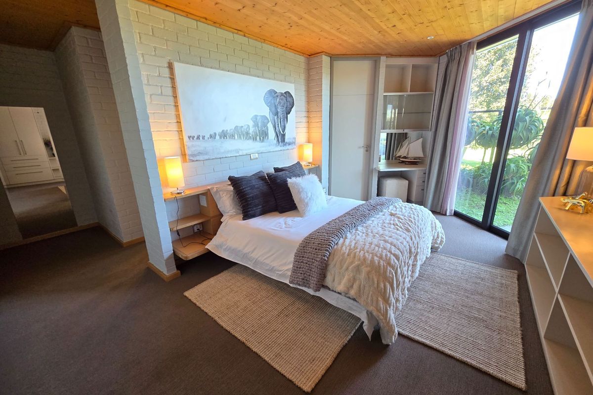 Spacious bedroom featuring a timber-clad ceiling, painted brick feature wall, built-in vanity, and large sliding glass doors providing natural light and garden access.