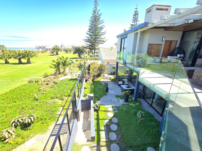 Elevated view of a modern rear exterior featuring a stone patio, glass balustrade, and a well-maintained garden overlooking a coastal landscape.