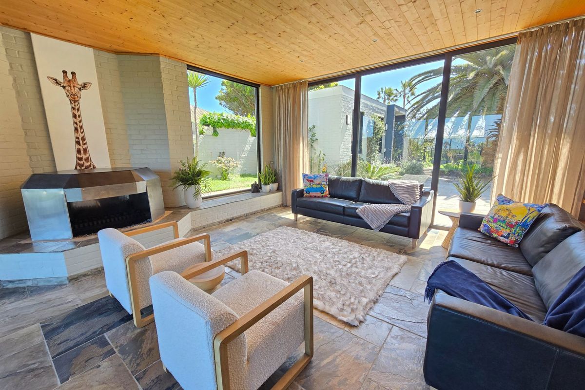 Spacious living room featuring a timber-clad ceiling, stone flooring, a unique built-in fireplace, and expansive floor-to-ceiling glass doors opening to the garden.