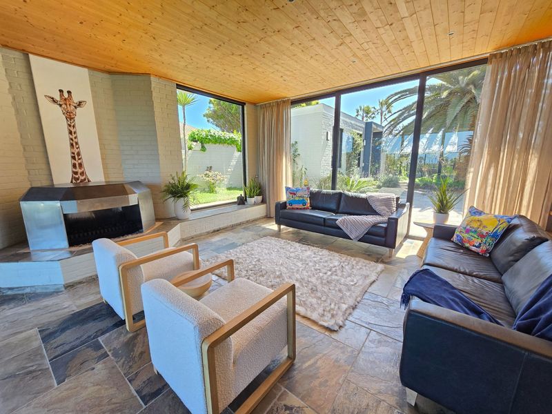 Spacious living room featuring a timber-clad ceiling, stone flooring, a unique built-in fireplace, and expansive floor-to-ceiling glass doors opening to the garden.