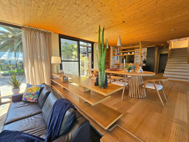 Spacious open-plan living and dining area featuring warm timber ceilings and flooring, large sliding glass doors, and a feature staircase.