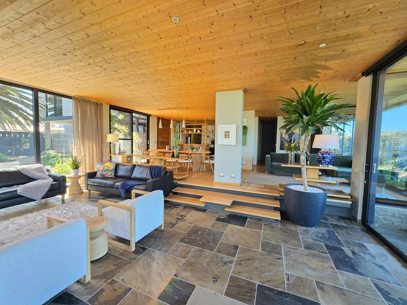 Spacious open-plan living and dining area featuring a warm timber-clad ceiling, natural stone flooring, and expansive sliding glass doors opening to the outdoors.